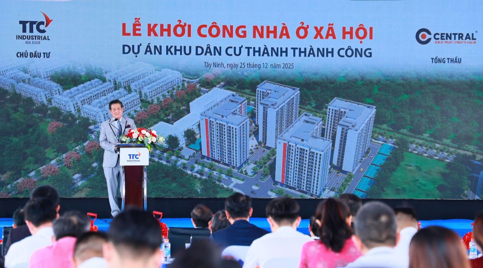 A person standing at a podium with a large screen with a picture of buildings and a large screen with textAI-generated content may be incorrect.